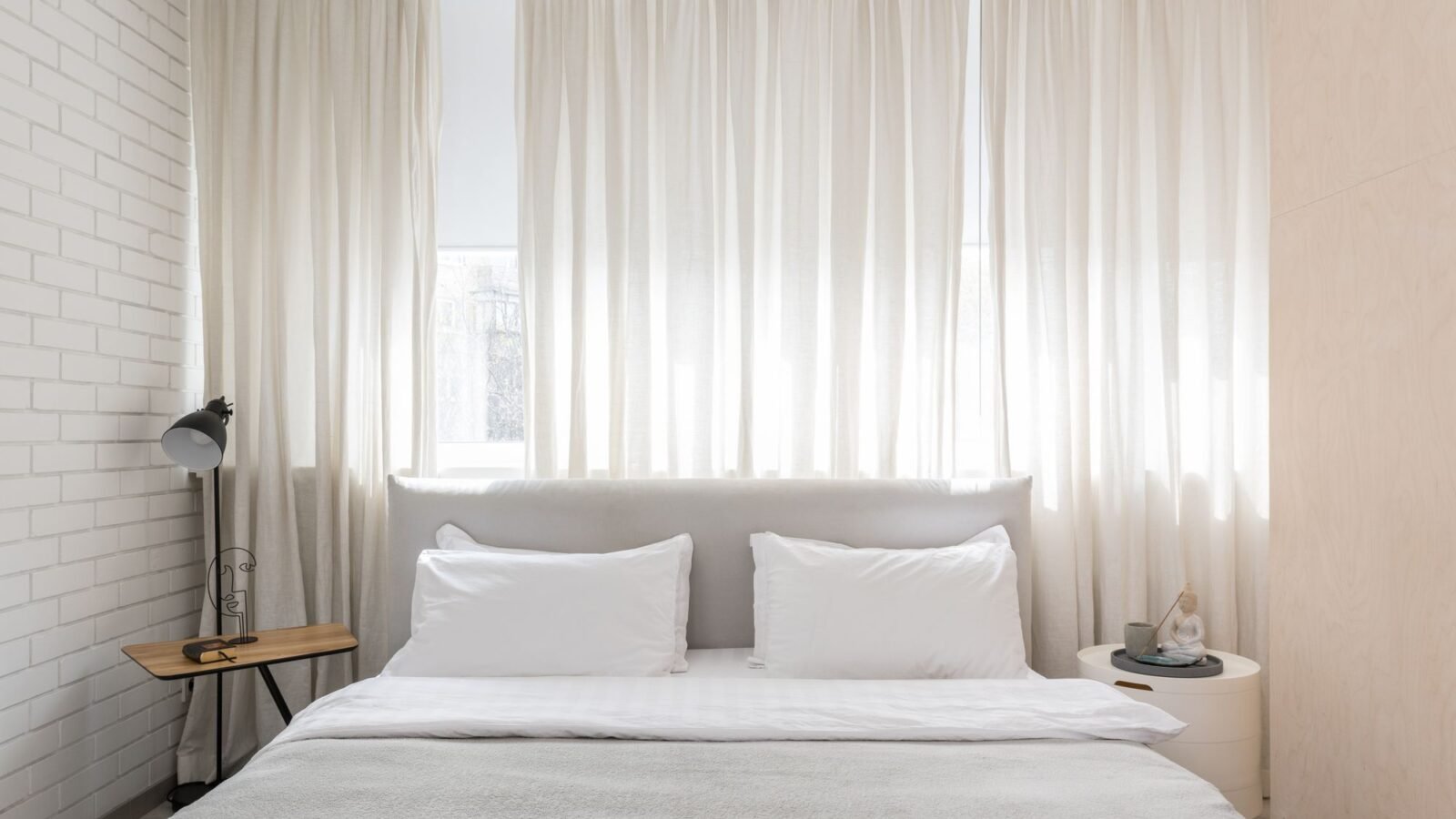 Small cozy bedroom with neutral bedding and warm bedside lighting.