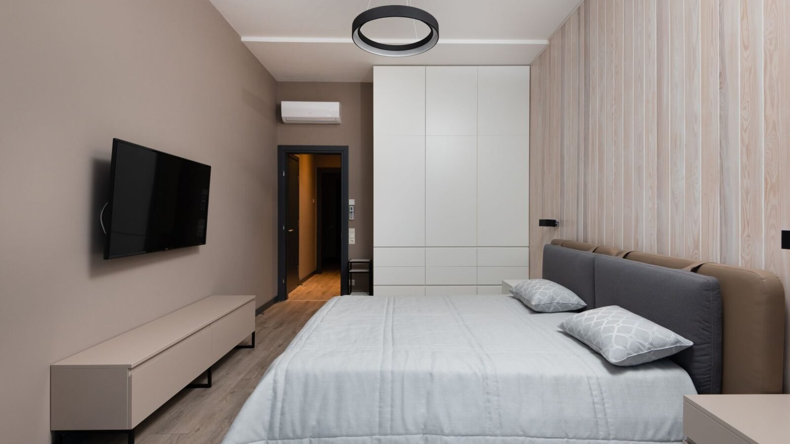 Modern bedroom with streamlined furniture, wardrobe storage, and wood flooring.