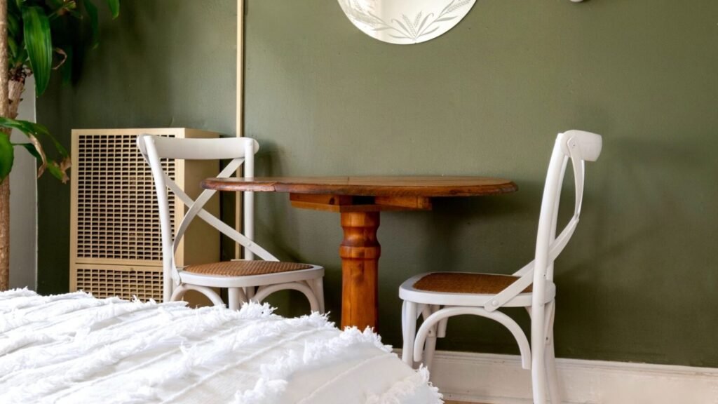 Bedroom with a sage green accent wall, natural wood flooring, white bedding, and plants.