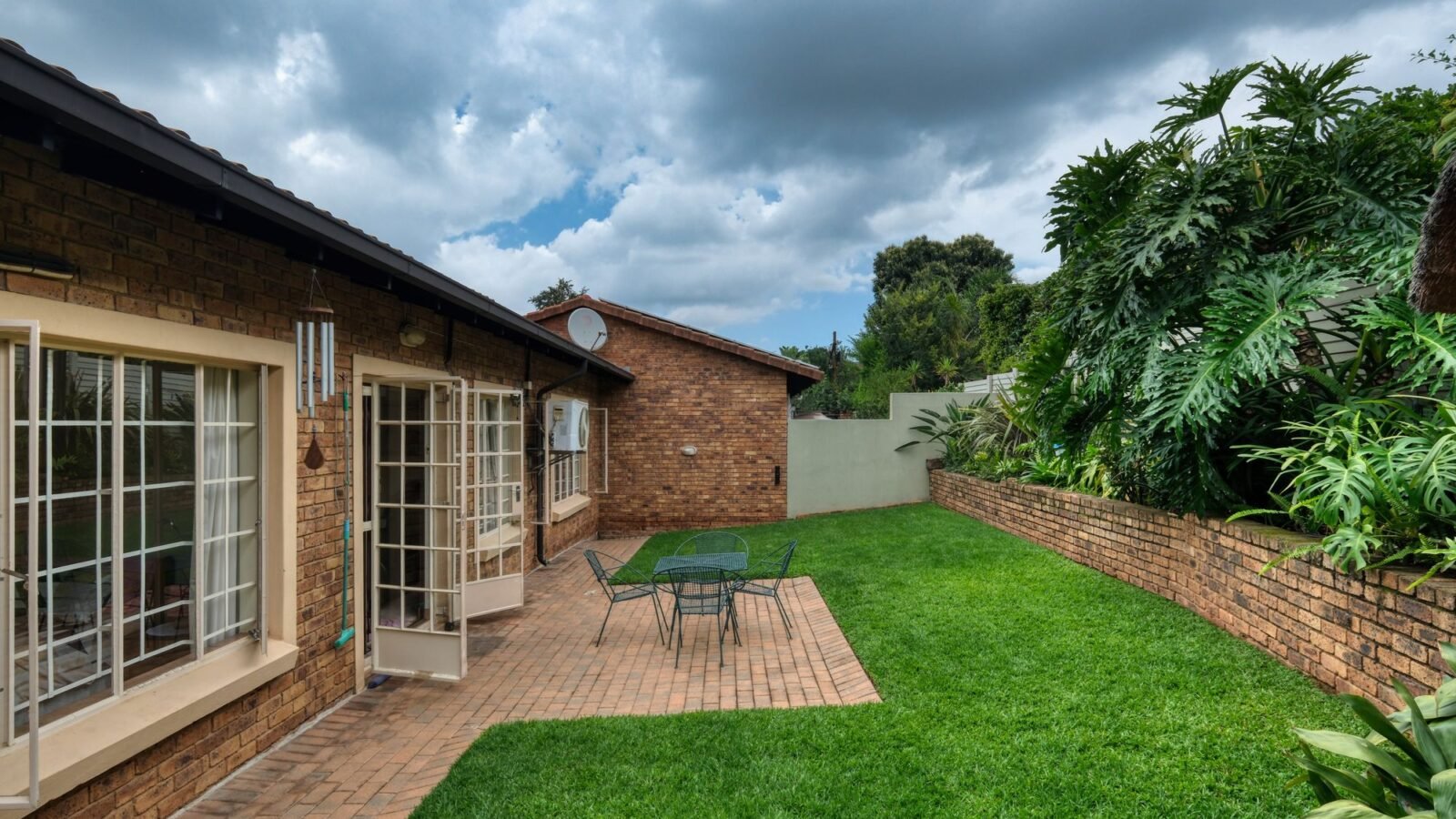 Cozy residential backyard with patio seating, lawn, and lush green planting.