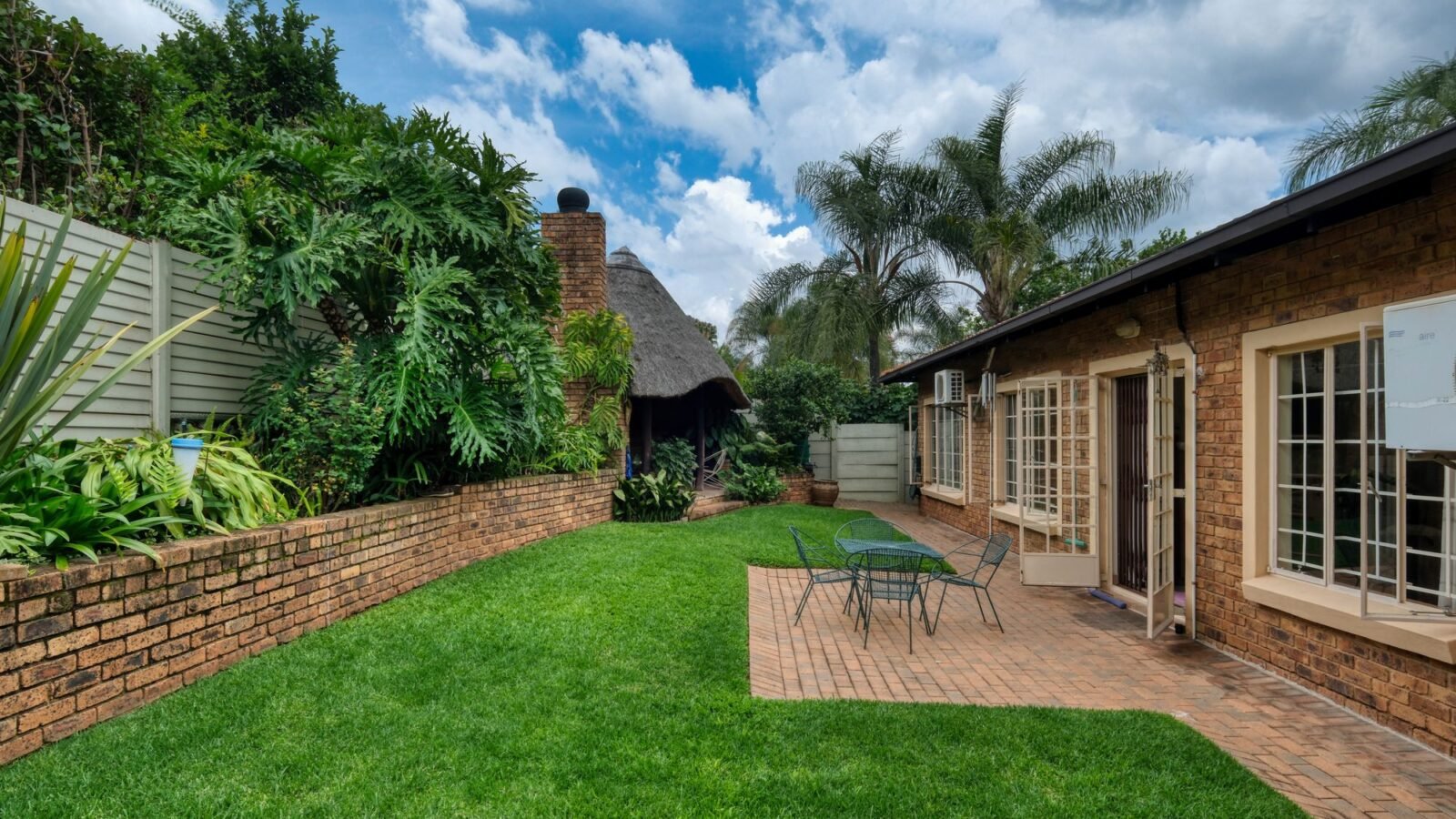 Compact backyard with outdoor table and chairs surrounded by greenery.