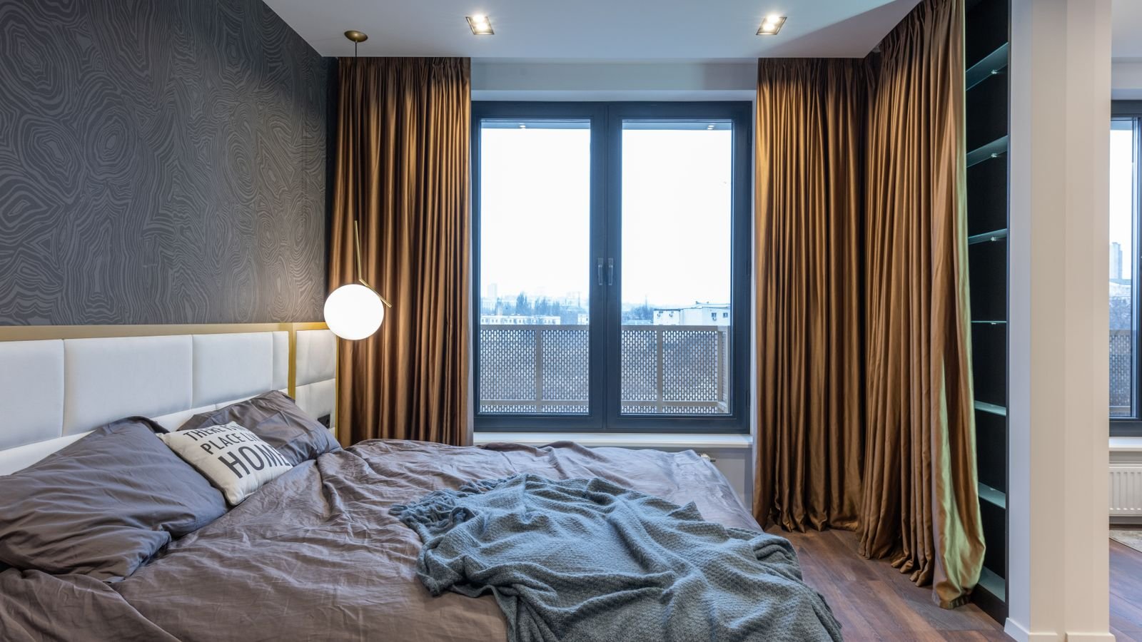 Bright bedroom with a bed beside a large window and full-length curtains.