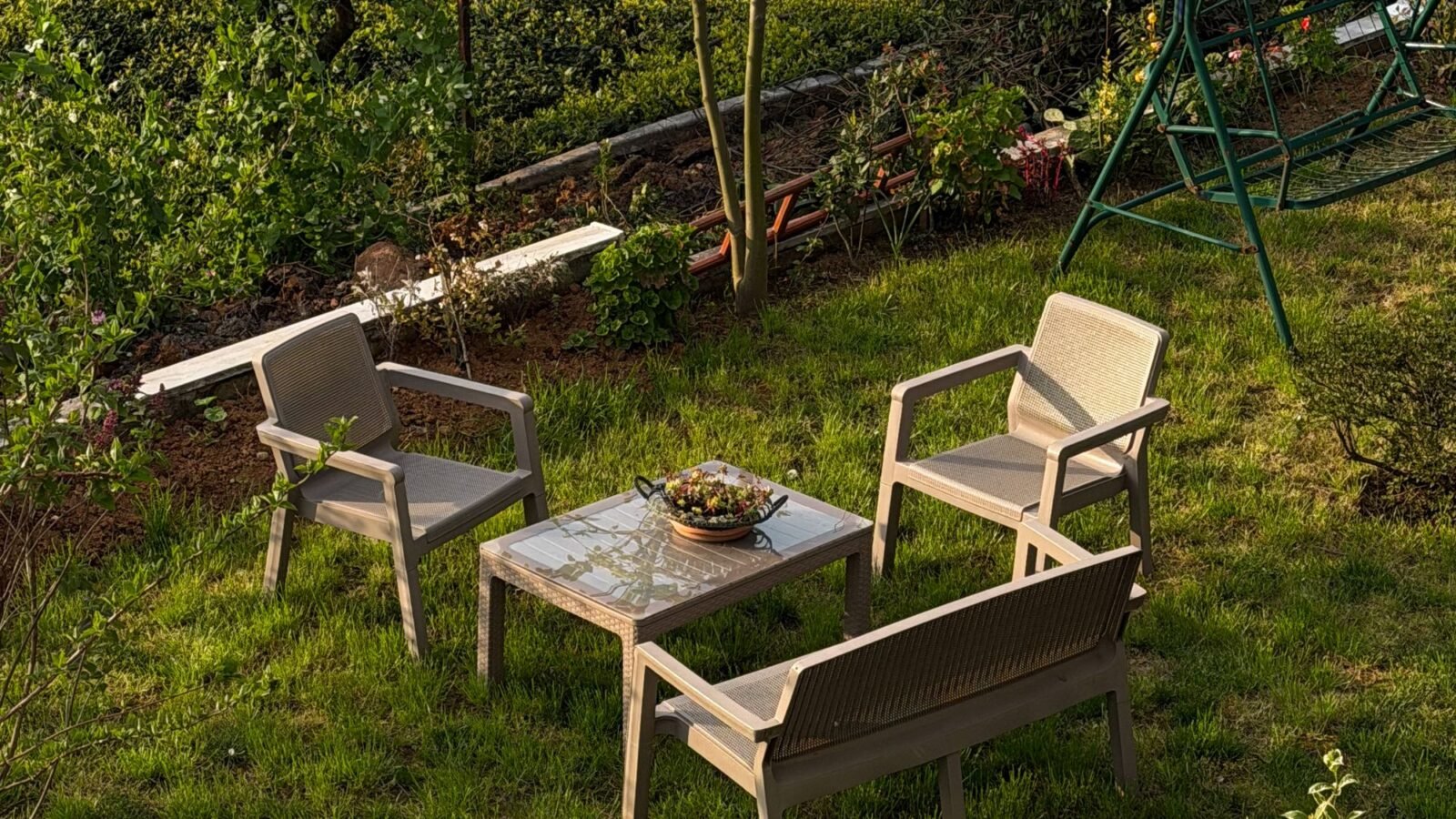 Sunlit small patio with chairs and table surrounded by garden greenery.