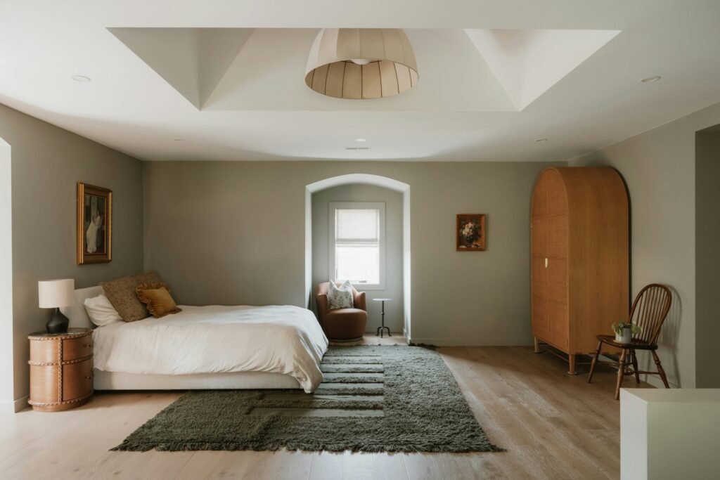 Warm neutral bedroom with cream bedding, natural wood furniture, a textured rug, and soft daylight.