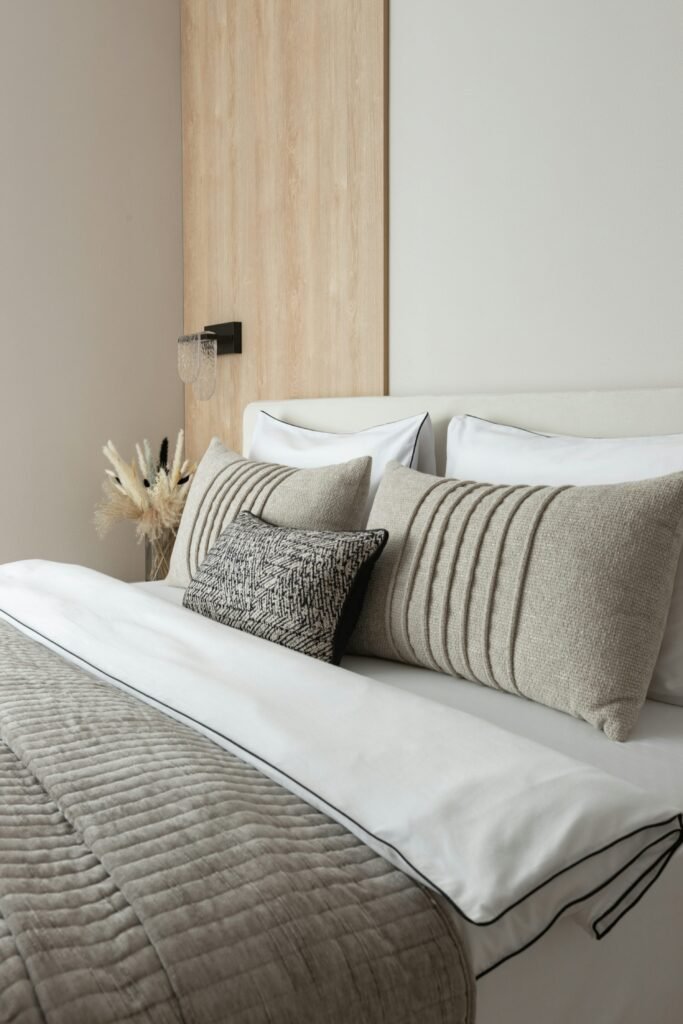 Warm neutral bedroom bed styled with cream sheets, taupe textured pillows, and layered beige bedding.