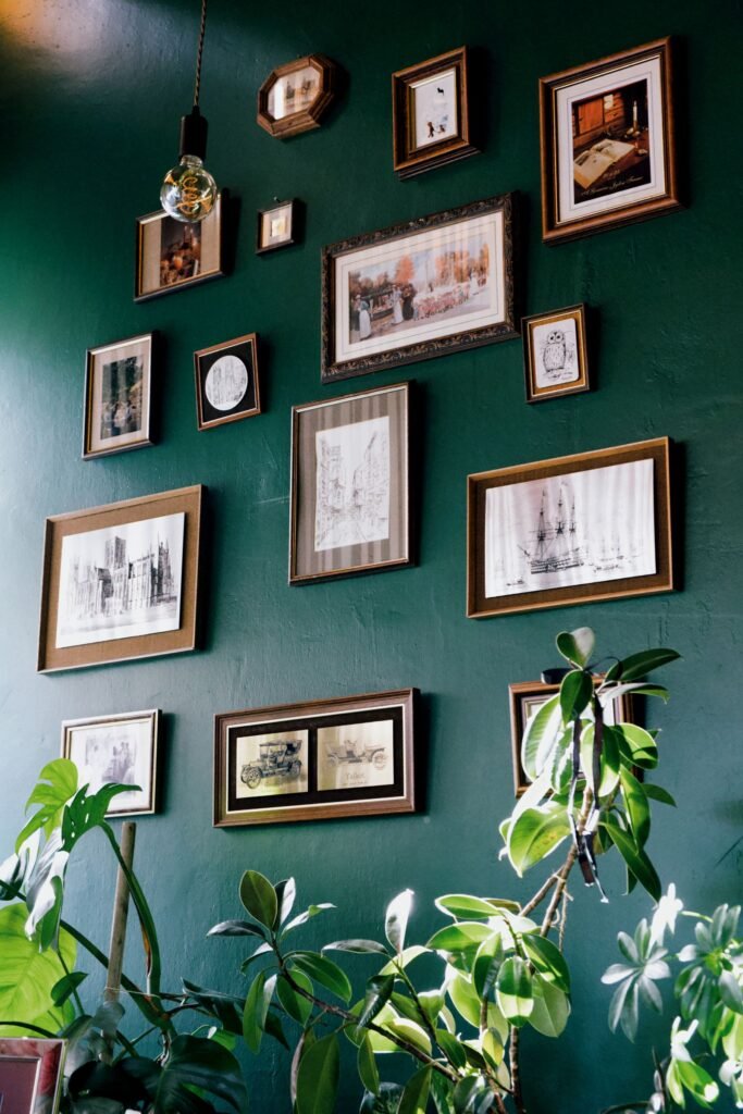 Gallery wall of framed art and prints on a green wall with plants